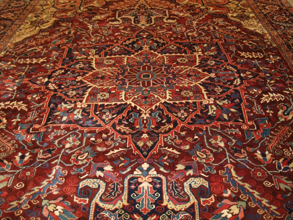 A large hand-knotted Persian Heriz wool carpet featuring a bold central geometric medallion in rust red, dark indigo, and ivory tones. View V