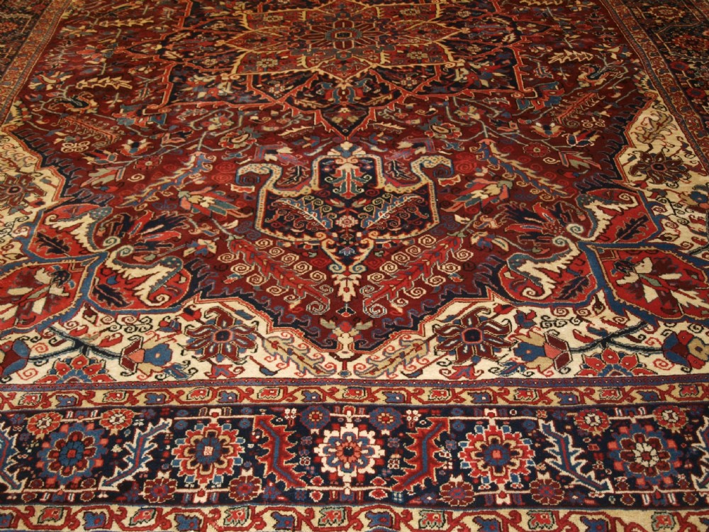 A large hand-knotted Persian Heriz wool carpet featuring a bold central geometric medallion in rust red, dark indigo, and ivory tones. View VI