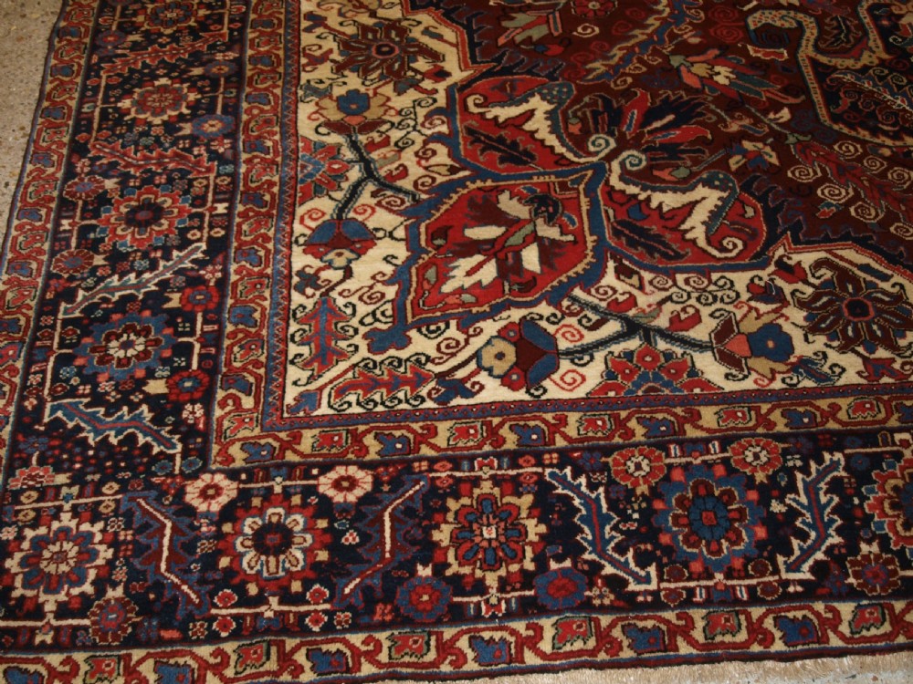 A large hand-knotted Persian Heriz wool carpet featuring a bold central geometric medallion in rust red, dark indigo, and ivory tones. View VII