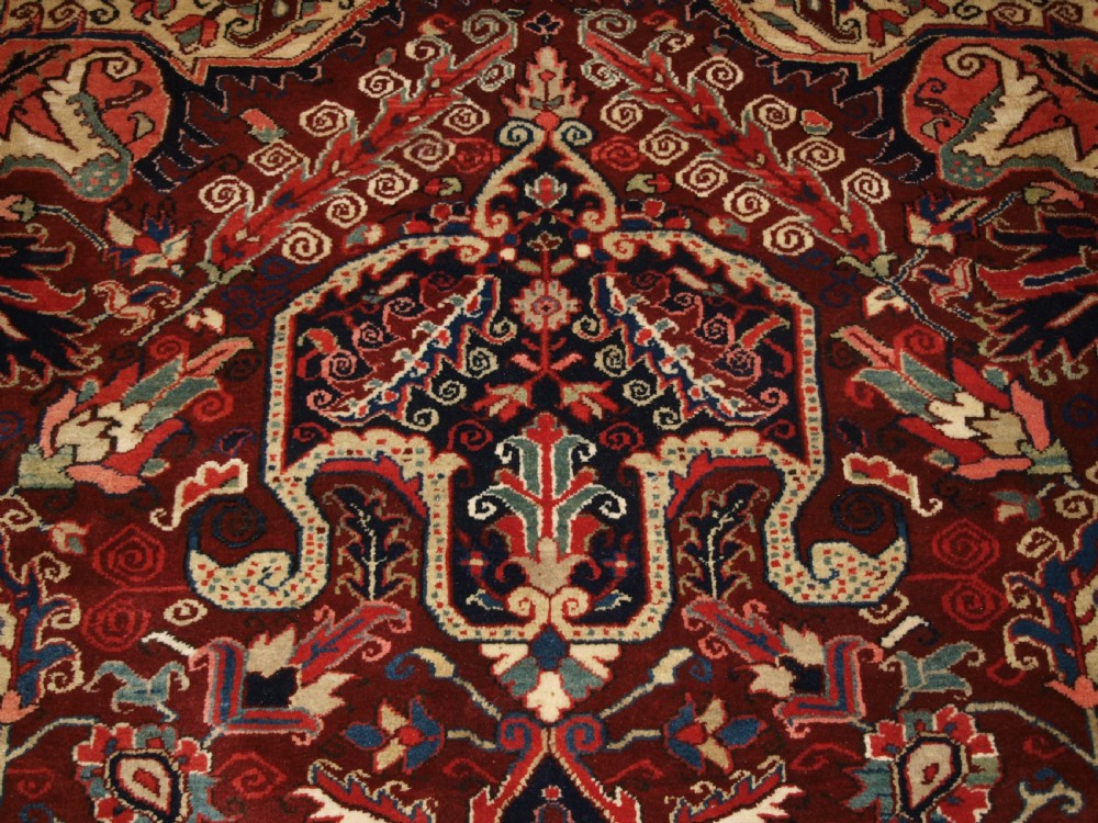A large hand-knotted Persian Heriz wool carpet featuring a bold central geometric medallion in rust red, dark indigo, and ivory tones. View VIII