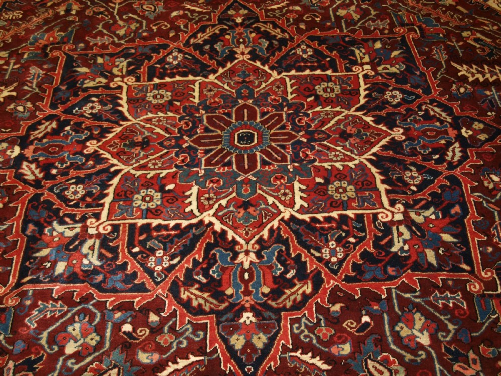 A large hand-knotted Persian Heriz wool carpet featuring a bold central geometric medallion in rust red, dark indigo, and ivory tones. View IX