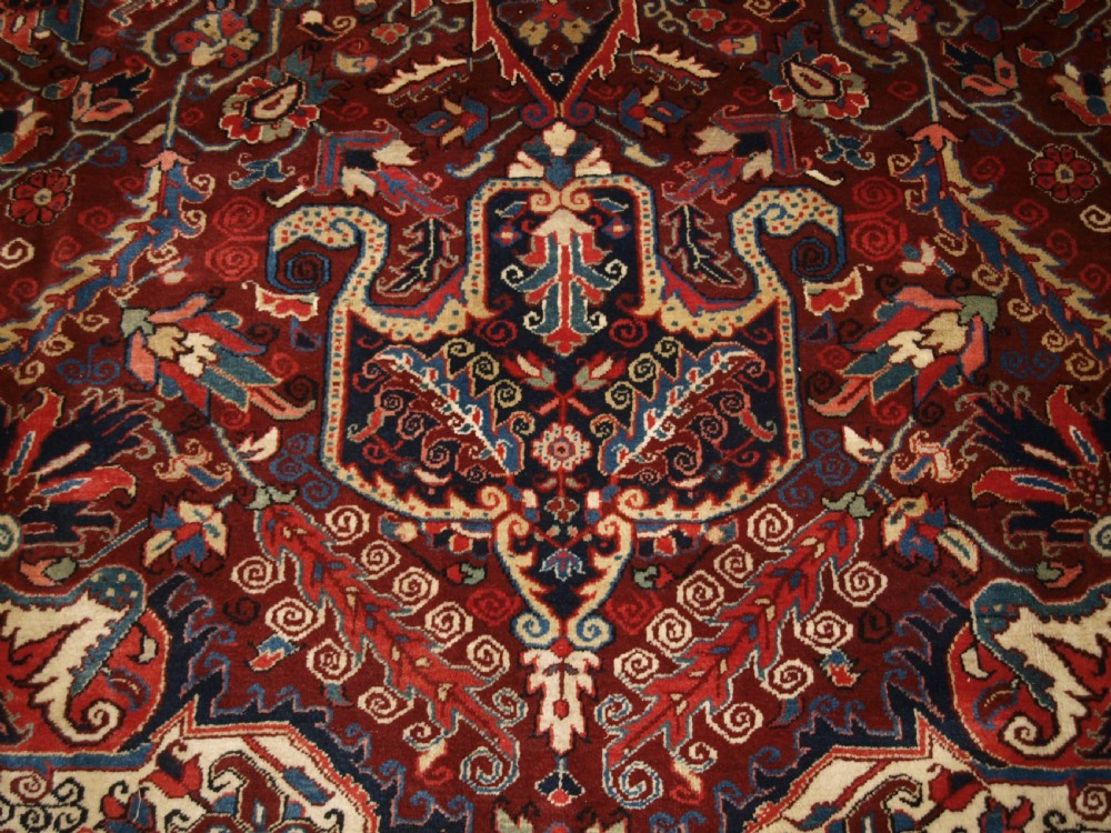 A large hand-knotted Persian Heriz wool carpet featuring a bold central geometric medallion in rust red, dark indigo, and ivory tones. View X