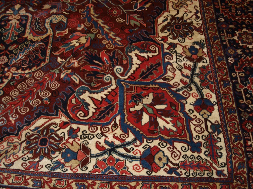 A large hand-knotted Persian Heriz wool carpet featuring a bold central geometric medallion in rust red, dark indigo, and ivory tones. View XI