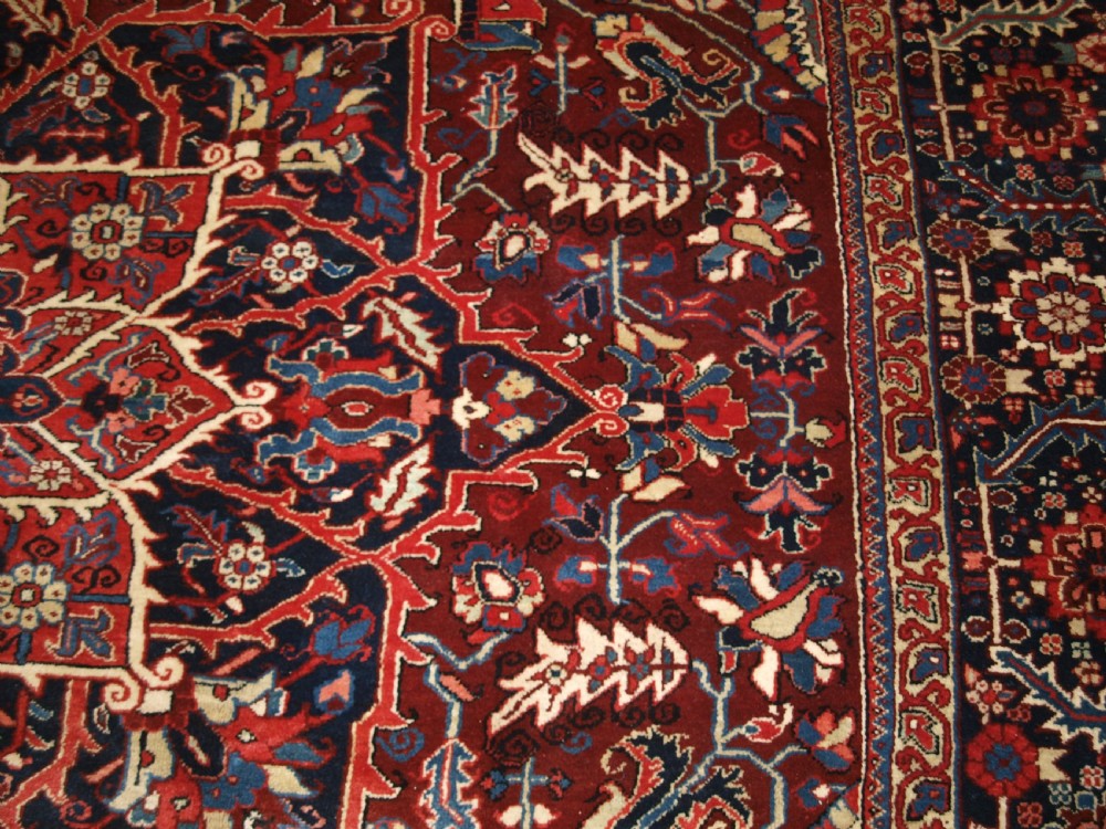 A large hand-knotted Persian Heriz wool carpet featuring a bold central geometric medallion in rust red, dark indigo, and ivory tones. View XII