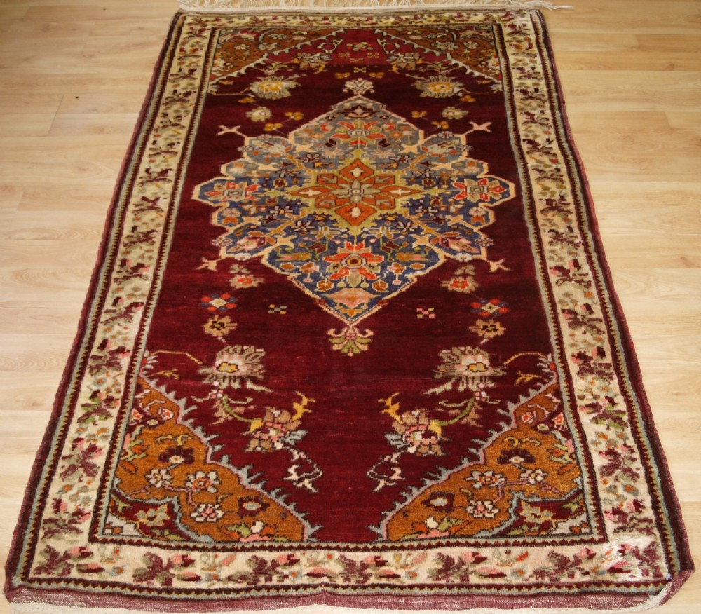 An antique hand-knotted Turkish Avanos wool rug featuring a deep burgundy red field with a central geometric medallion and cream floral border.