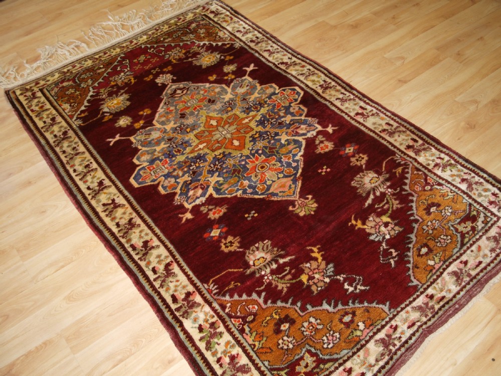 An antique hand-knotted Turkish Avanos wool rug featuring a deep burgundy red field with a central geometric medallion and cream floral border. View II