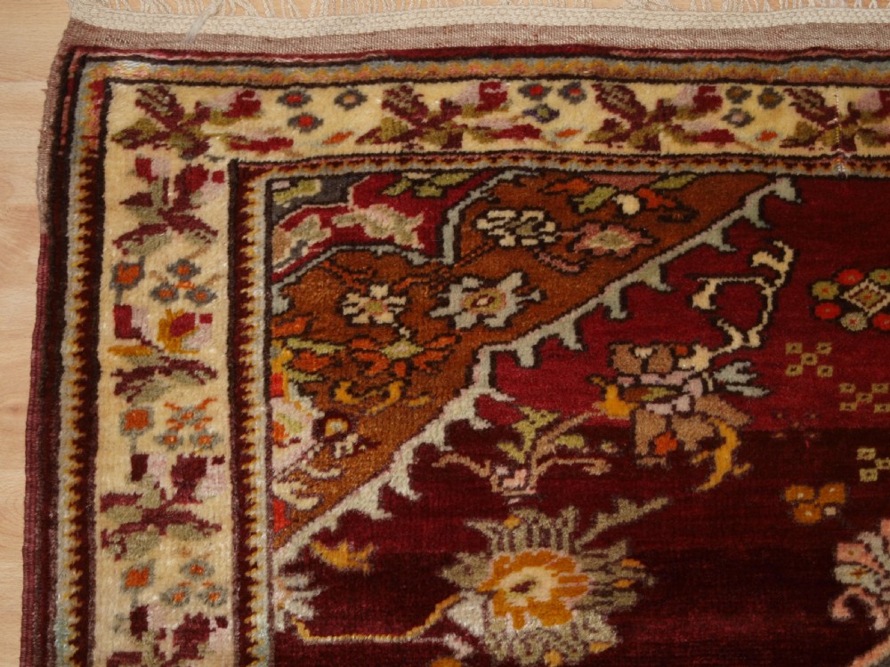 An antique hand-knotted Turkish Avanos wool rug featuring a deep burgundy red field with a central geometric medallion and cream floral border. View III