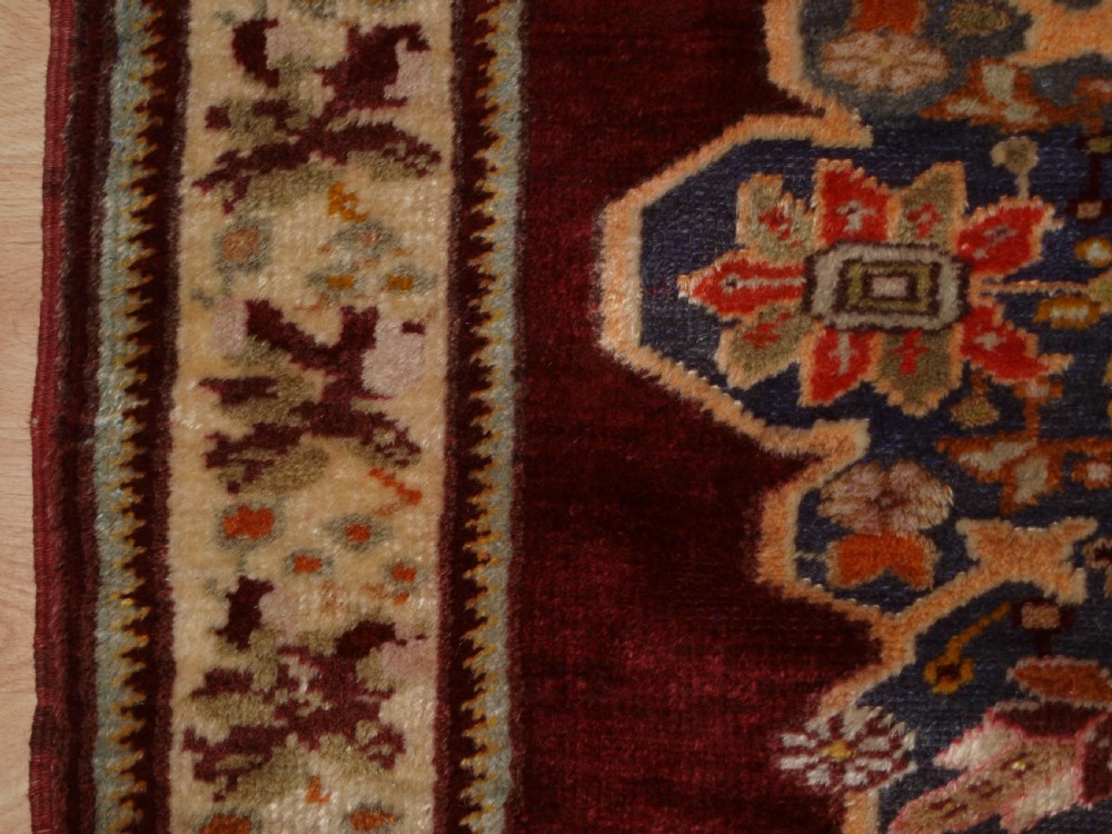 An antique hand-knotted Turkish Avanos wool rug featuring a deep burgundy red field with a central geometric medallion and cream floral border. View IV