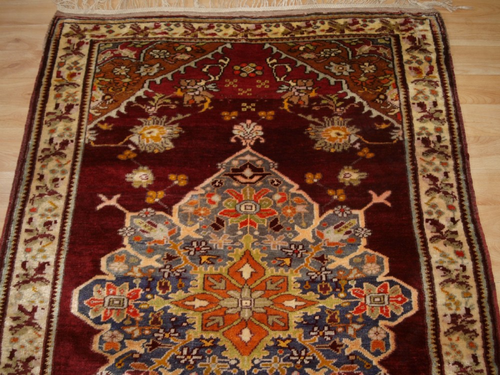An antique hand-knotted Turkish Avanos wool rug featuring a deep burgundy red field with a central geometric medallion and cream floral border. View V