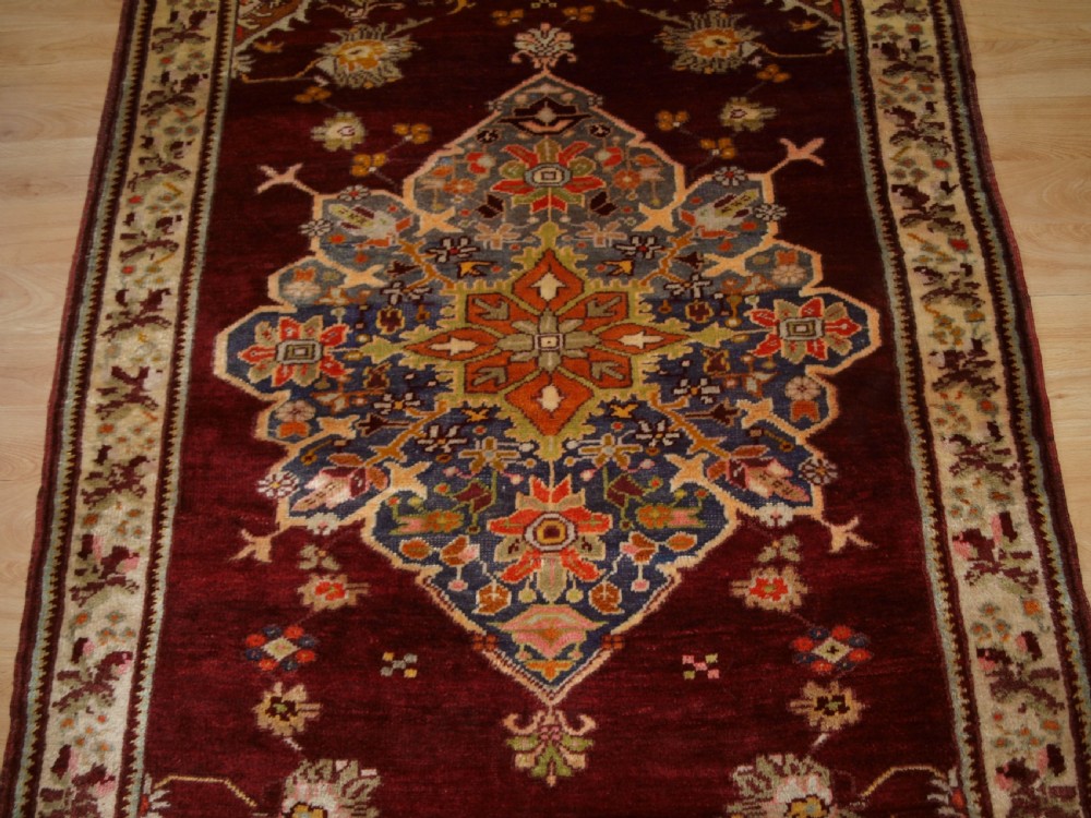 An antique hand-knotted Turkish Avanos wool rug featuring a deep burgundy red field with a central geometric medallion and cream floral border. View VI
