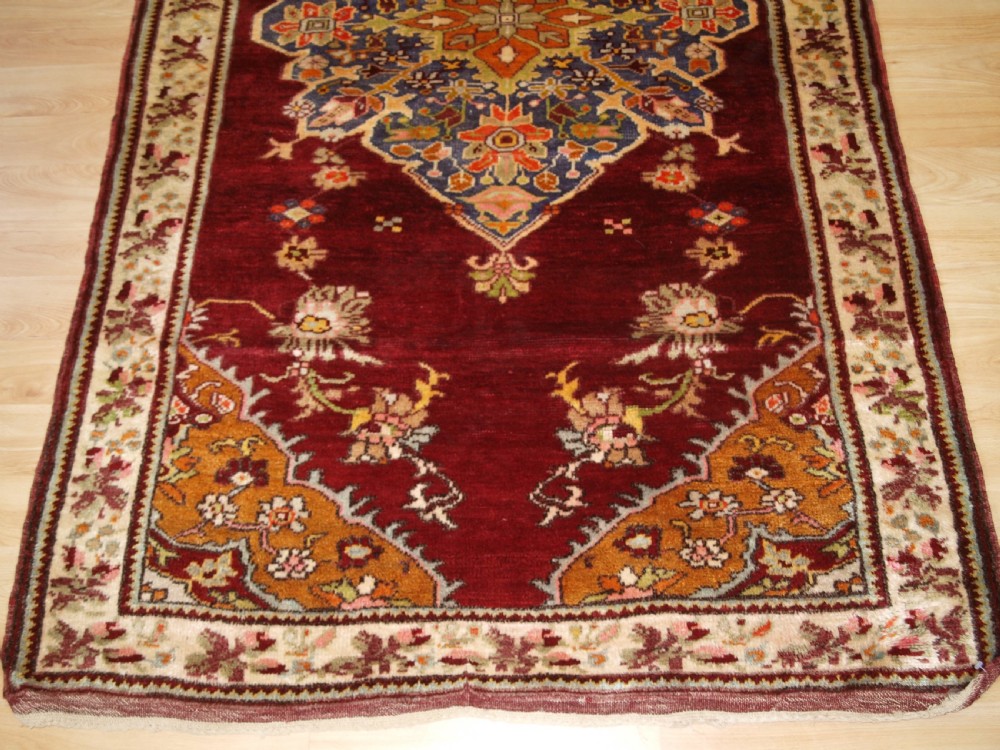 An antique hand-knotted Turkish Avanos wool rug featuring a deep burgundy red field with a central geometric medallion and cream floral border. View VII