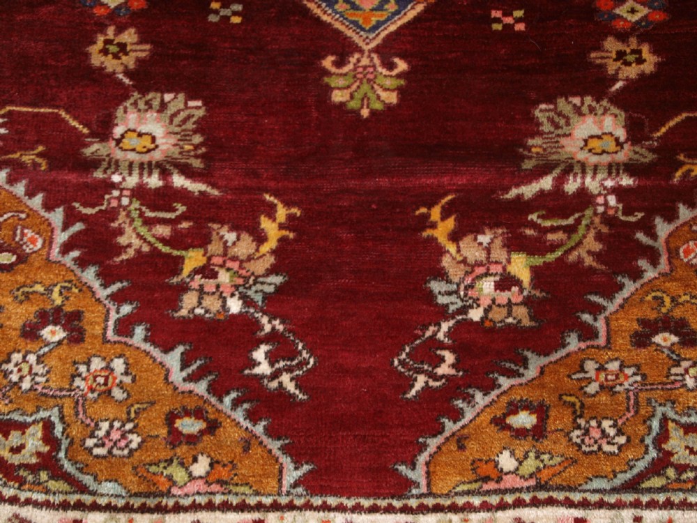 An antique hand-knotted Turkish Avanos wool rug featuring a deep burgundy red field with a central geometric medallion and cream floral border. View X
