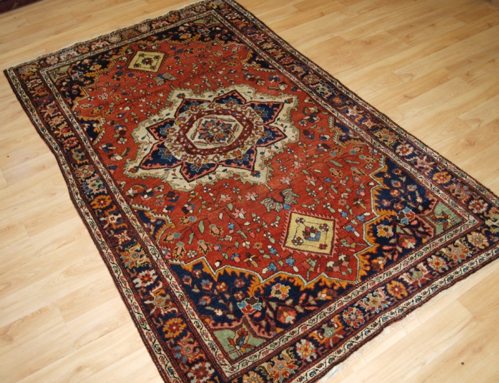 A hand-knotted antique Persian Sarouk wool rug with a prominent central star medallion, floral motifs, terracotta red field, and navy blue border. View II