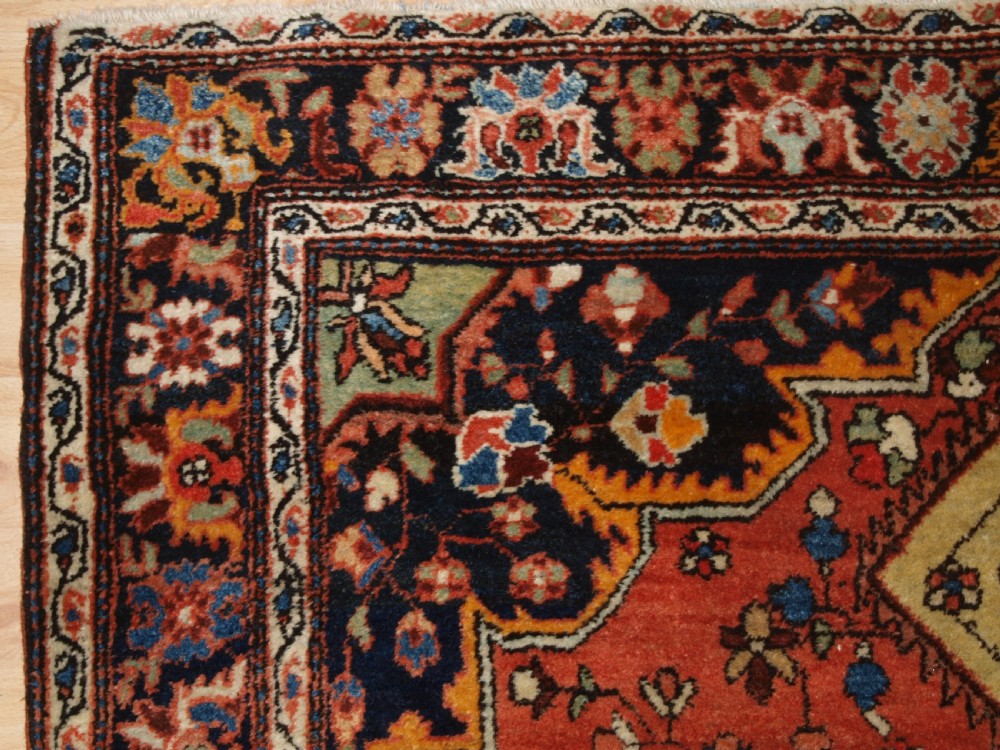 A hand-knotted antique Persian Sarouk wool rug with a prominent central star medallion, floral motifs, terracotta red field, and navy blue border. View III