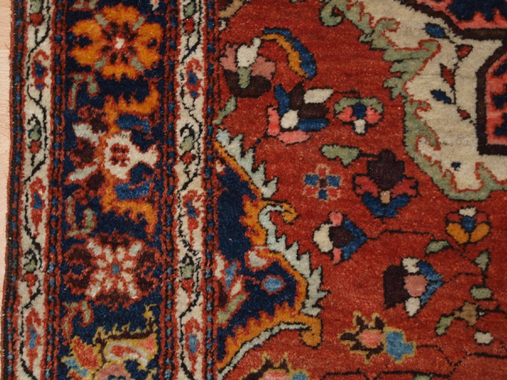 A hand-knotted antique Persian Sarouk wool rug with a prominent central star medallion, floral motifs, terracotta red field, and navy blue border. View IV