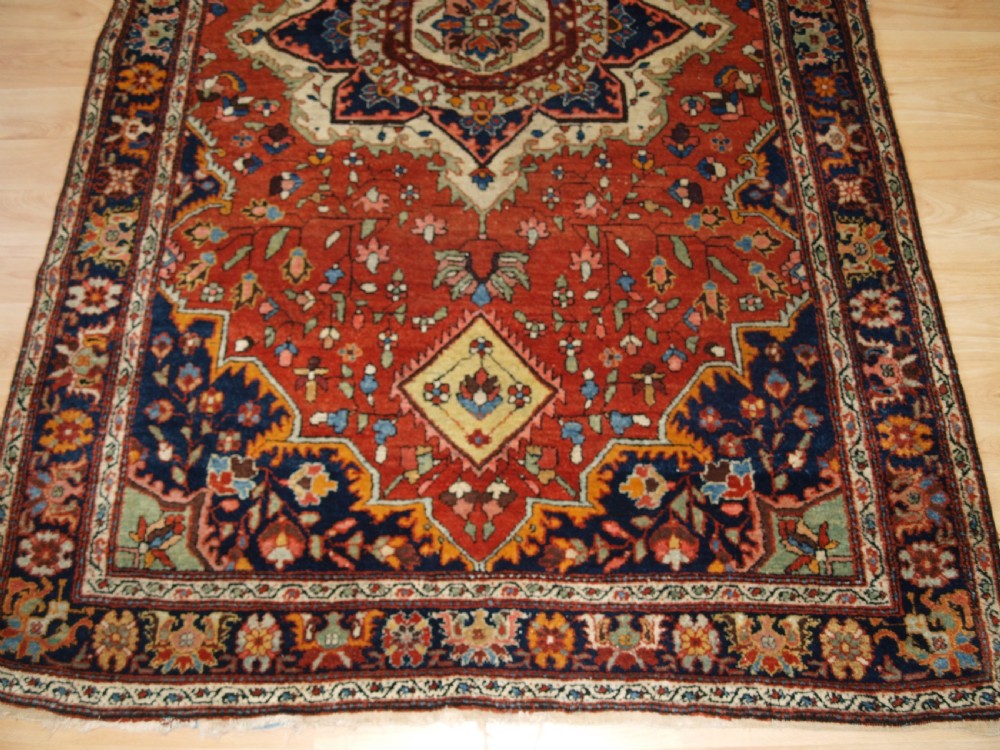 A hand-knotted antique Persian Sarouk wool rug with a prominent central star medallion, floral motifs, terracotta red field, and navy blue border. View VIII