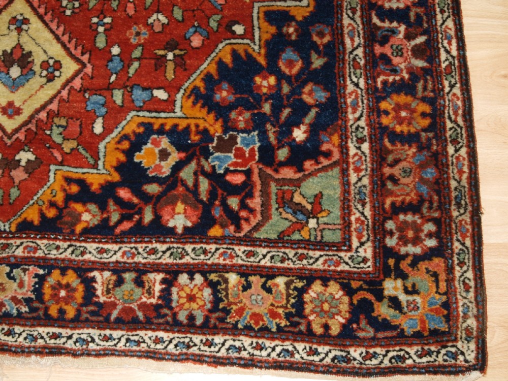 A hand-knotted antique Persian Sarouk wool rug with a prominent central star medallion, floral motifs, terracotta red field, and navy blue border. View XI