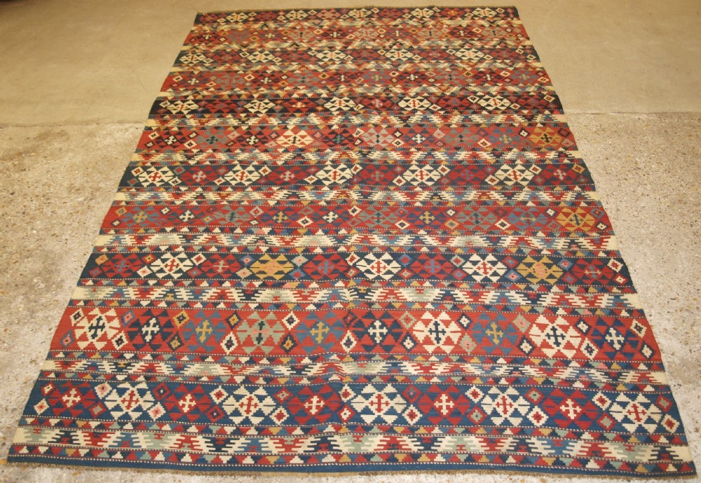 An antique flatweave wool kilim featuring horizontal bands filled with geometric diamond and cross motifs in red, navy blue, ivory, and yellow tones.