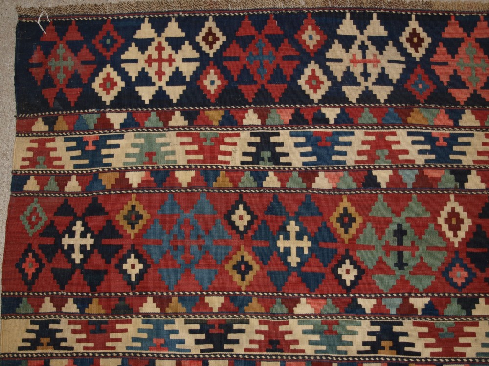 An antique flatweave wool kilim featuring horizontal bands filled with geometric diamond and cross motifs in red, navy blue, ivory, and yellow tones. View II