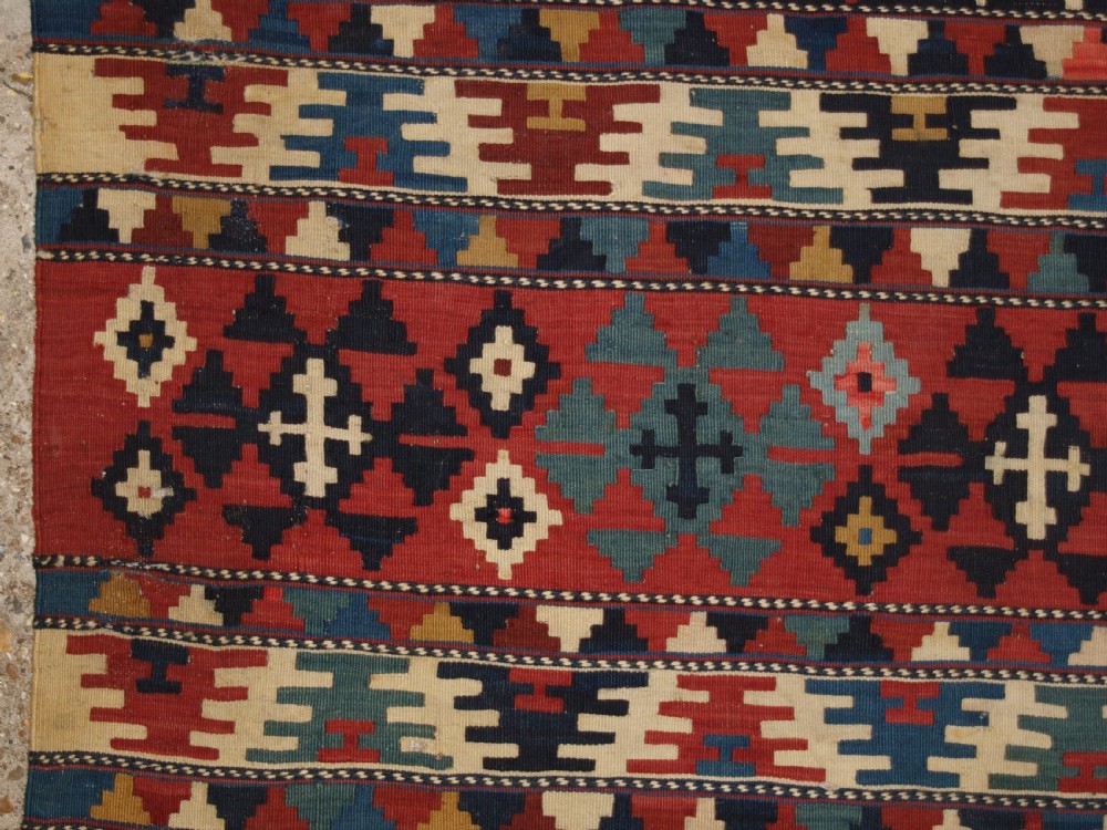 An antique flatweave wool kilim featuring horizontal bands filled with geometric diamond and cross motifs in red, navy blue, ivory, and yellow tones. View III