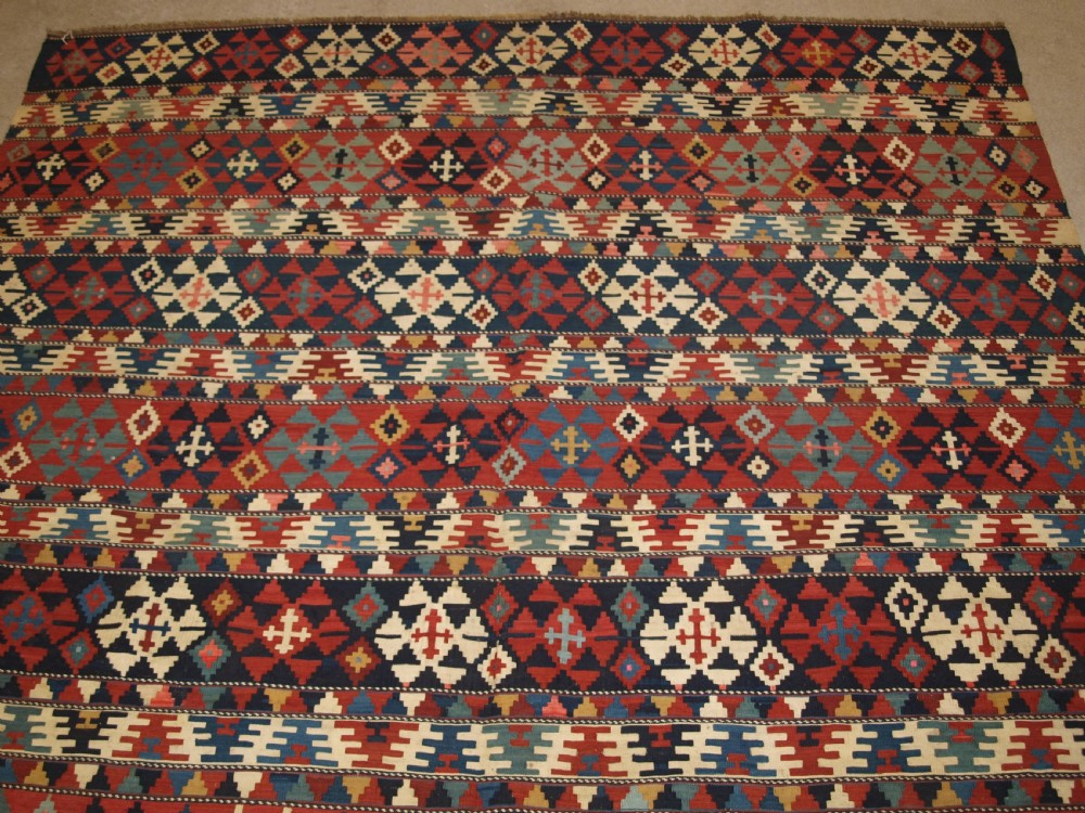 An antique flatweave wool kilim featuring horizontal bands filled with geometric diamond and cross motifs in red, navy blue, ivory, and yellow tones. View IV