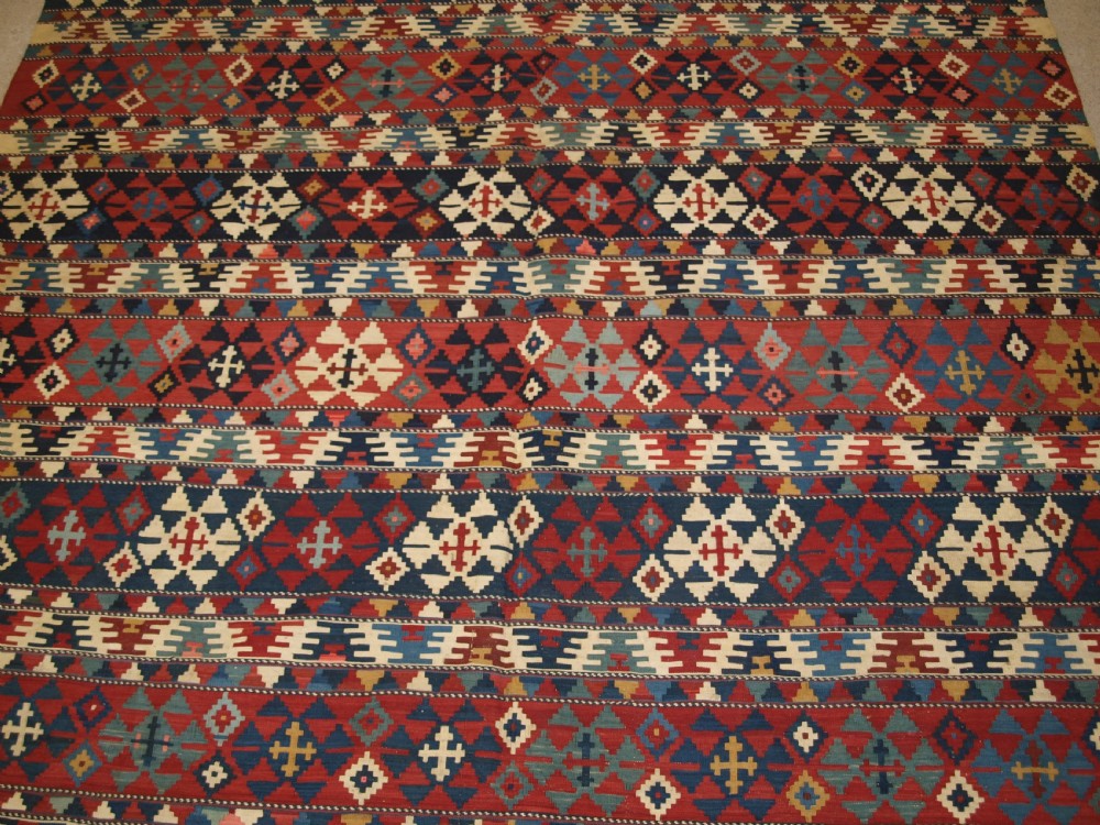 An antique flatweave wool kilim featuring horizontal bands filled with geometric diamond and cross motifs in red, navy blue, ivory, and yellow tones. View V