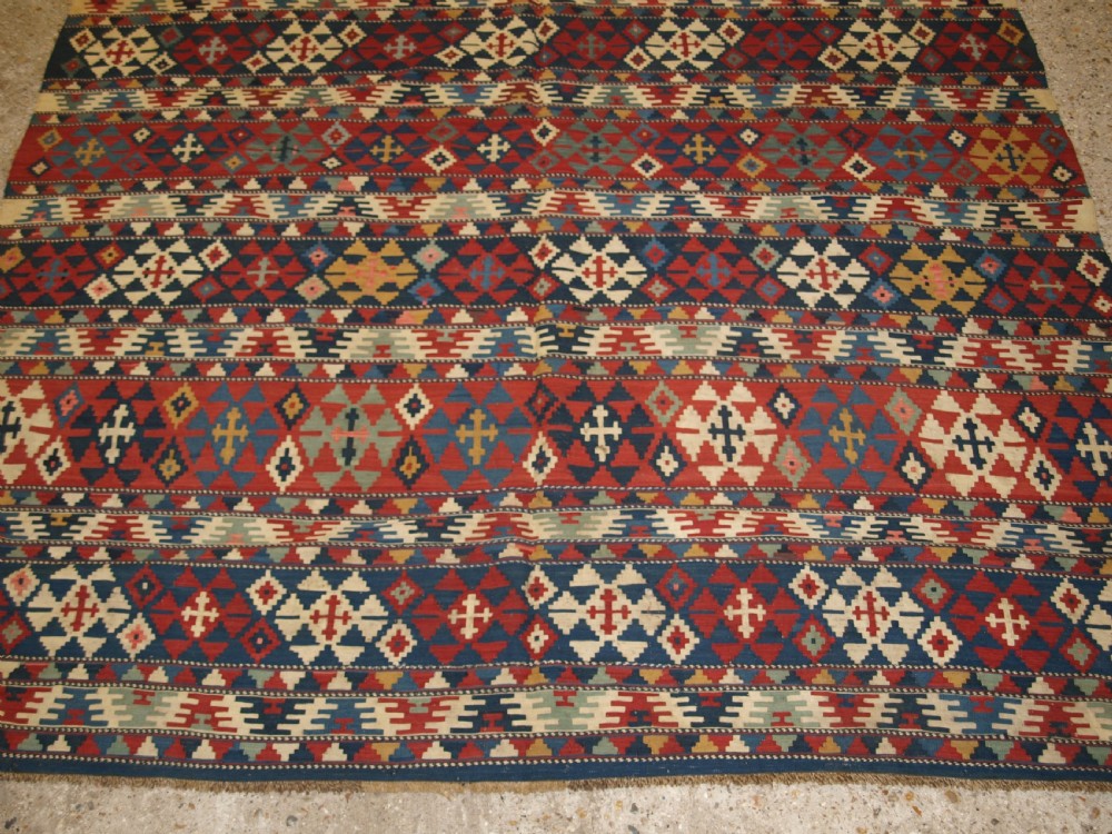 An antique flatweave wool kilim featuring horizontal bands filled with geometric diamond and cross motifs in red, navy blue, ivory, and yellow tones. View VII