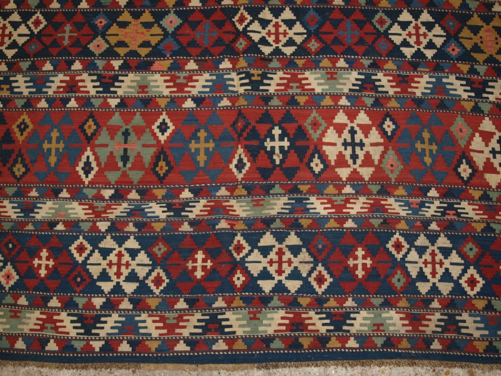 An antique flatweave wool kilim featuring horizontal bands filled with geometric diamond and cross motifs in red, navy blue, ivory, and yellow tones. View X