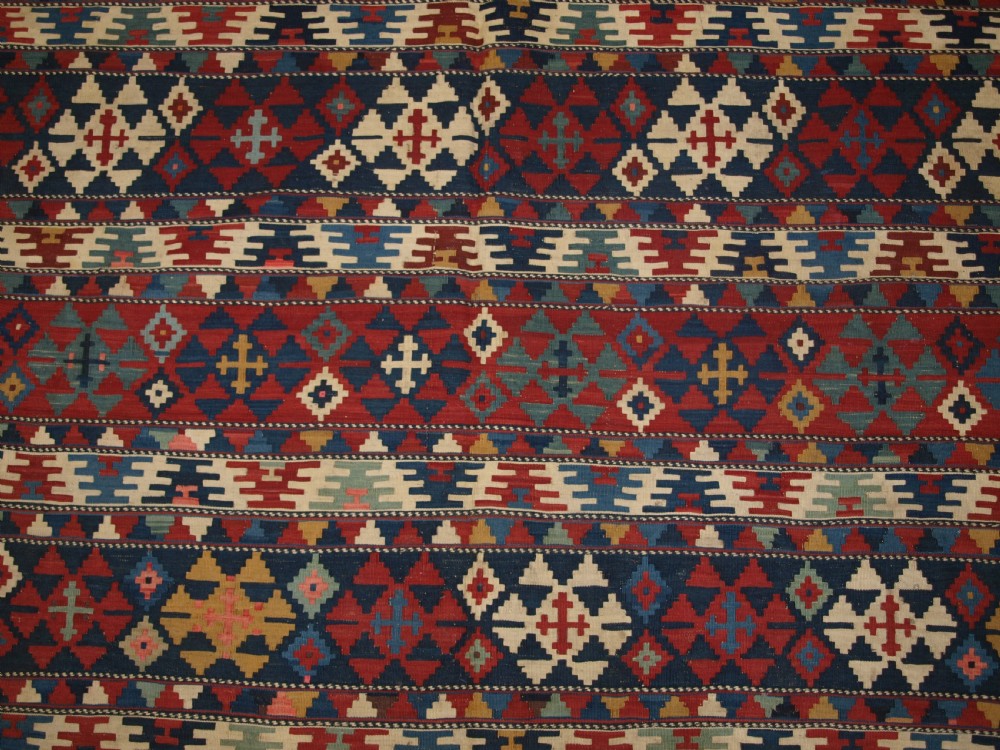 An antique flatweave wool kilim featuring horizontal bands filled with geometric diamond and cross motifs in red, navy blue, ivory, and yellow tones. View XI