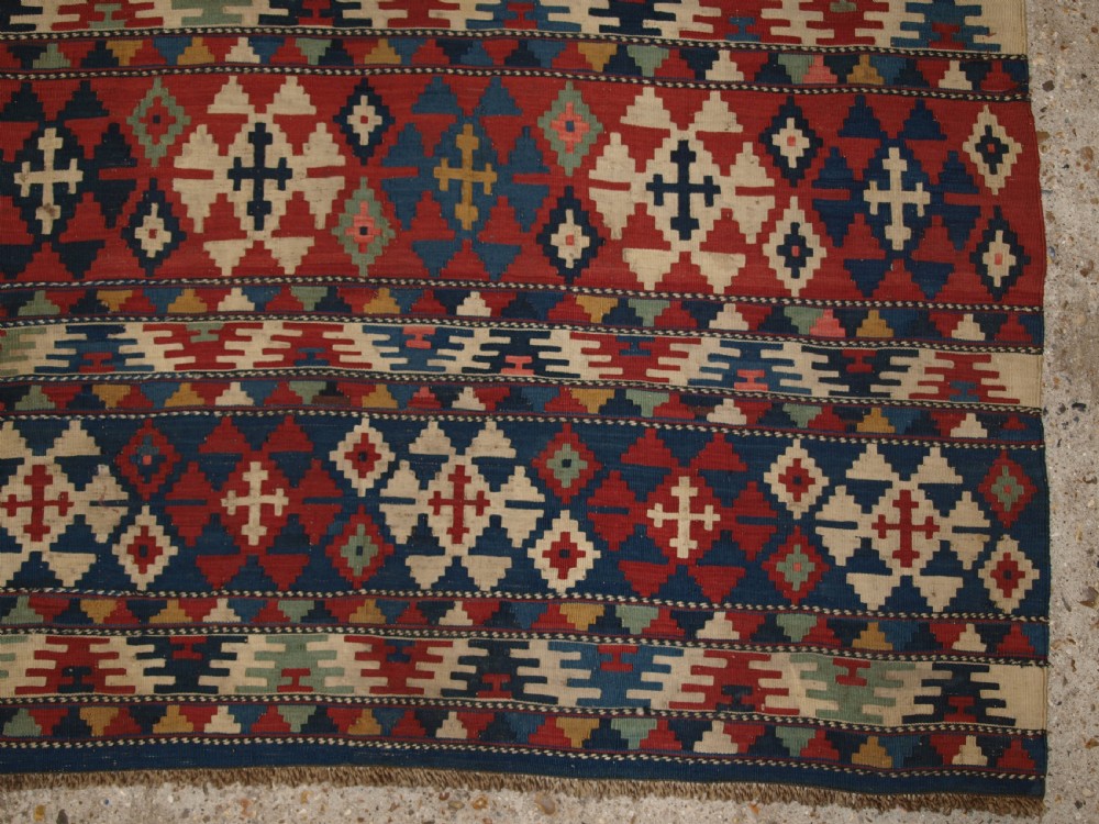 An antique flatweave wool kilim featuring horizontal bands filled with geometric diamond and cross motifs in red, navy blue, ivory, and yellow tones. View XII