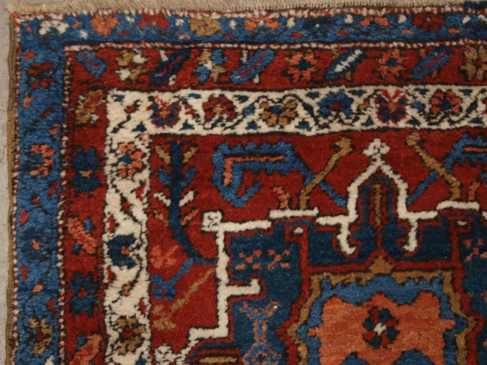 An antique Persian Karaja long runner rug featuring geometric hooked medallions on a terracotta red field framed by ivory and navy blue decorative borders. View III