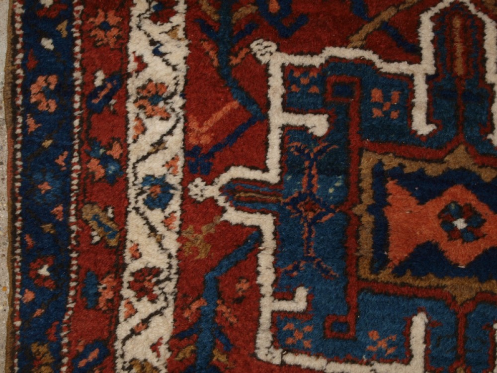 An antique Persian Karaja long runner rug featuring geometric hooked medallions on a terracotta red field framed by ivory and navy blue decorative borders. View IV