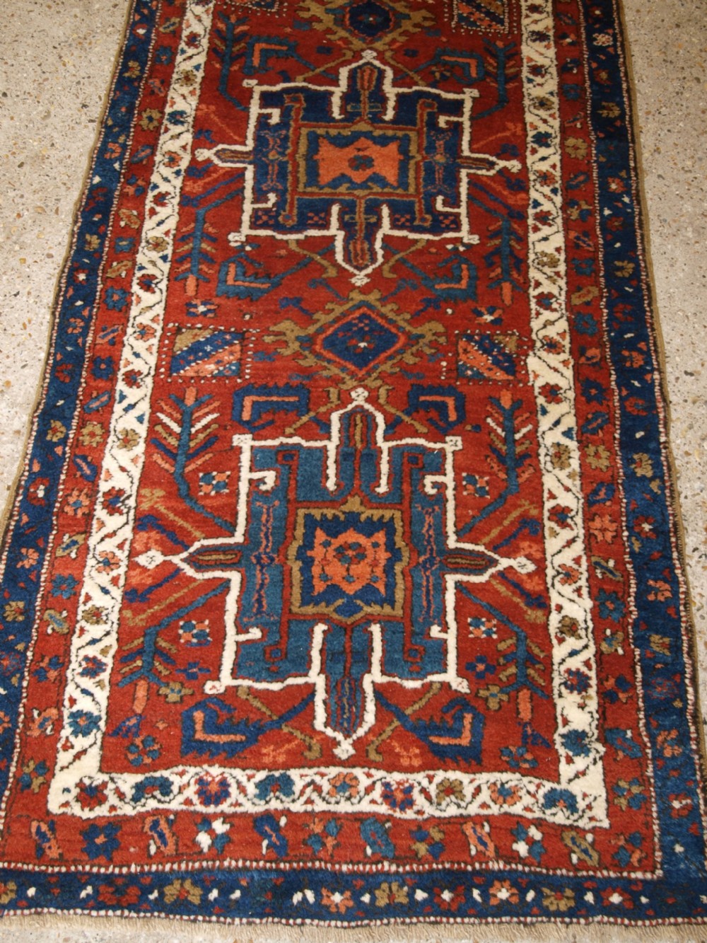 An antique Persian Karaja long runner rug featuring geometric hooked medallions on a terracotta red field framed by ivory and navy blue decorative borders. View VII
