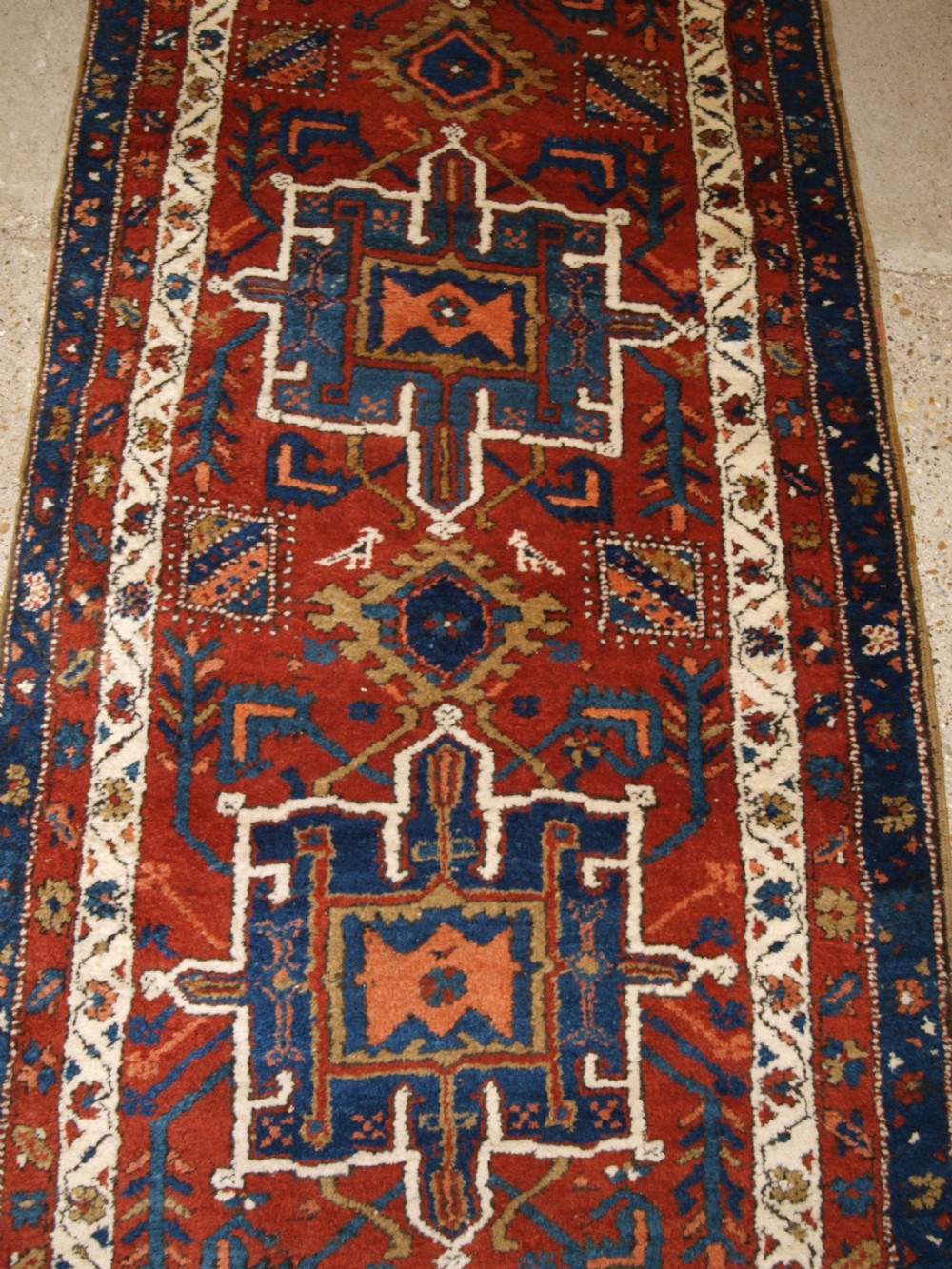 An antique Persian Karaja long runner rug featuring geometric hooked medallions on a terracotta red field framed by ivory and navy blue decorative borders. View VIII