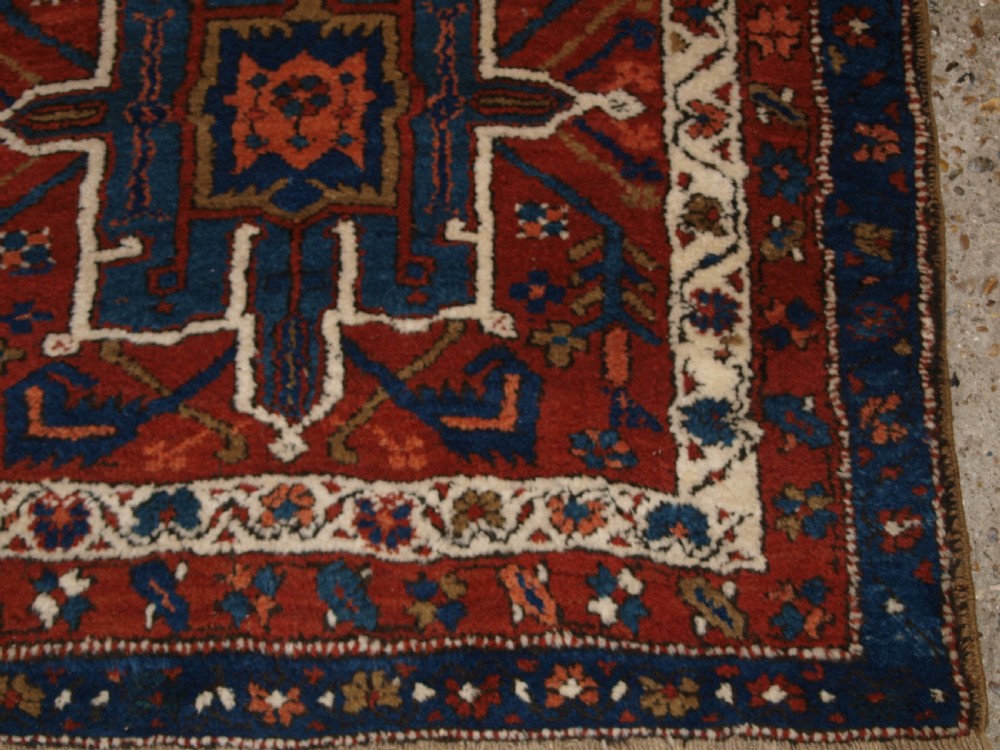 An antique Persian Karaja long runner rug featuring geometric hooked medallions on a terracotta red field framed by ivory and navy blue decorative borders. View IX