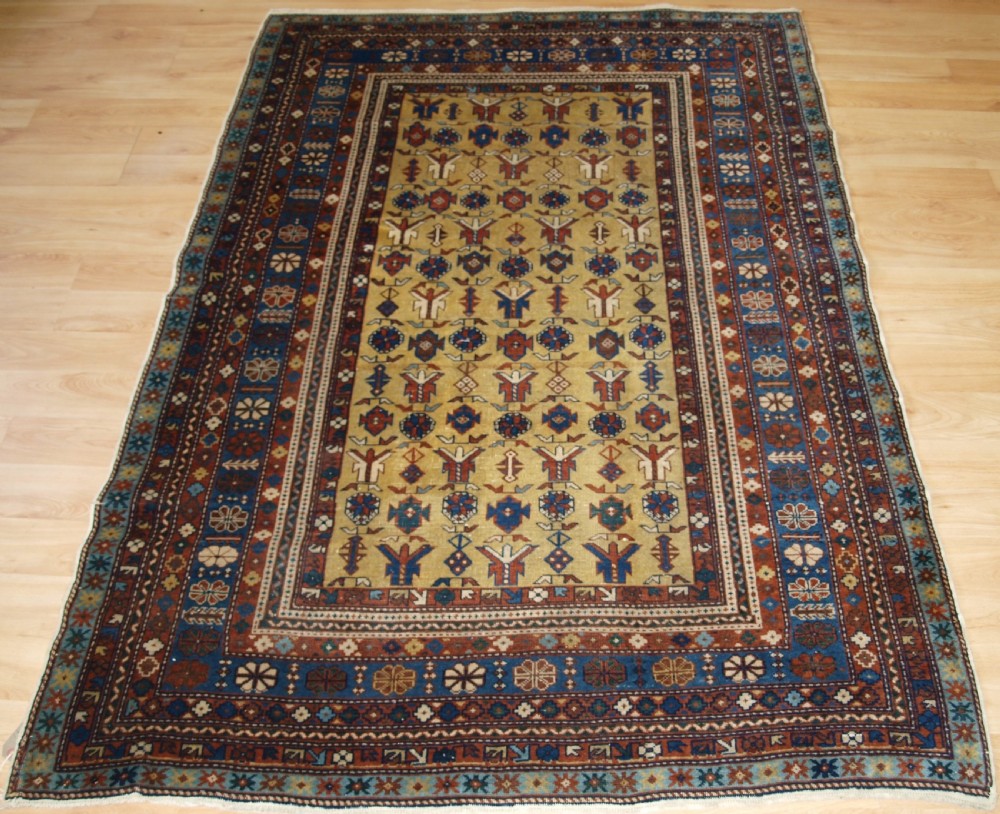 A hand-knotted wool rug featuring a central yellow field decorated with geometric motifs, enclosed by multi-tiered navy blue and terracotta patterned borders.
