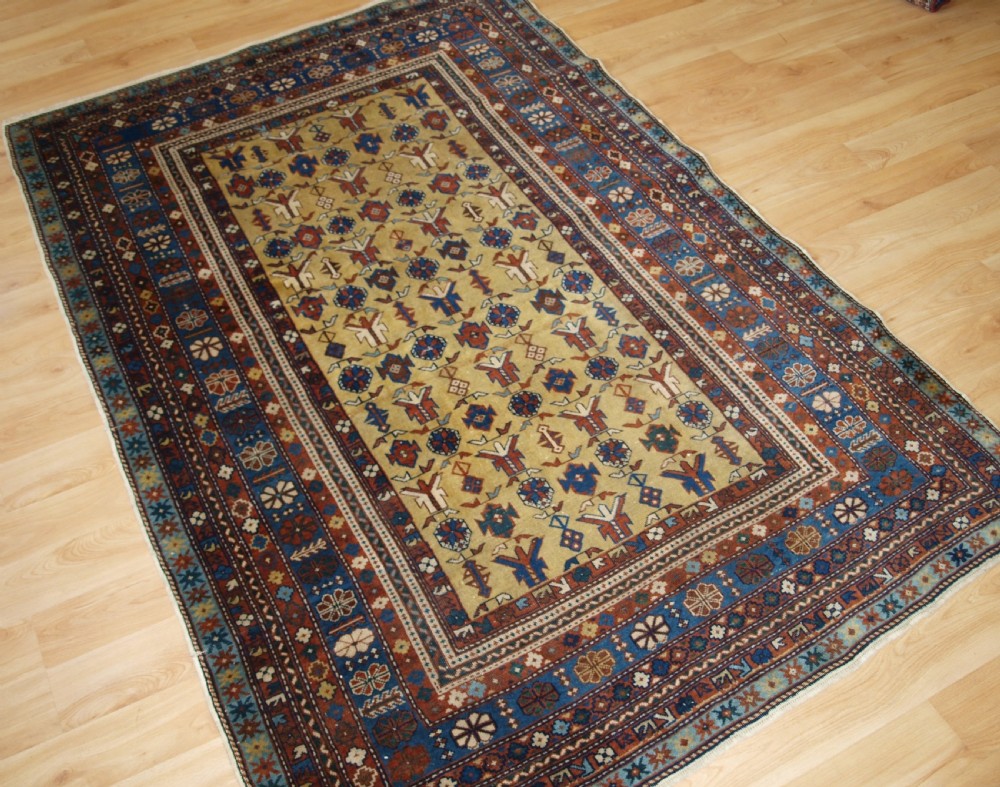 A hand-knotted wool rug featuring a central yellow field decorated with geometric motifs, enclosed by multi-tiered navy blue and terracotta patterned borders. View II