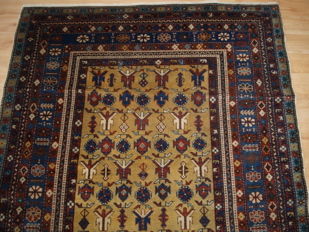 A hand-knotted wool rug featuring a central yellow field decorated with geometric motifs, enclosed by multi-tiered navy blue and terracotta patterned borders. View IV