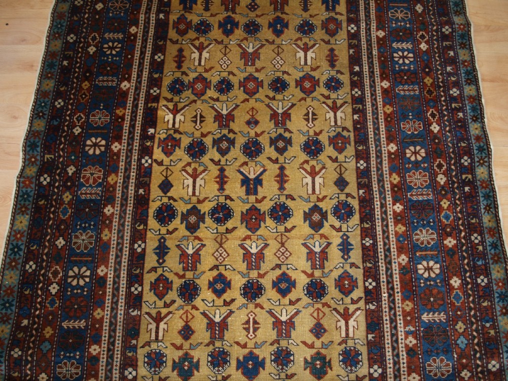 A hand-knotted wool rug featuring a central yellow field decorated with geometric motifs, enclosed by multi-tiered navy blue and terracotta patterned borders. View V