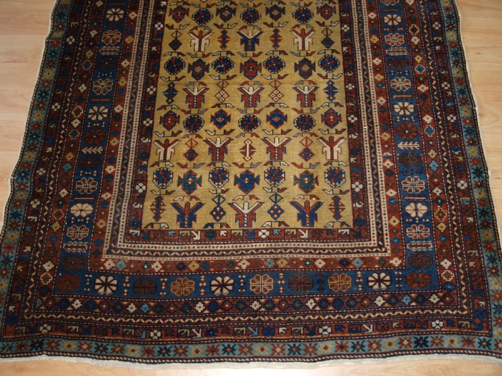 A hand-knotted wool rug featuring a central yellow field decorated with geometric motifs, enclosed by multi-tiered navy blue and terracotta patterned borders. View VI