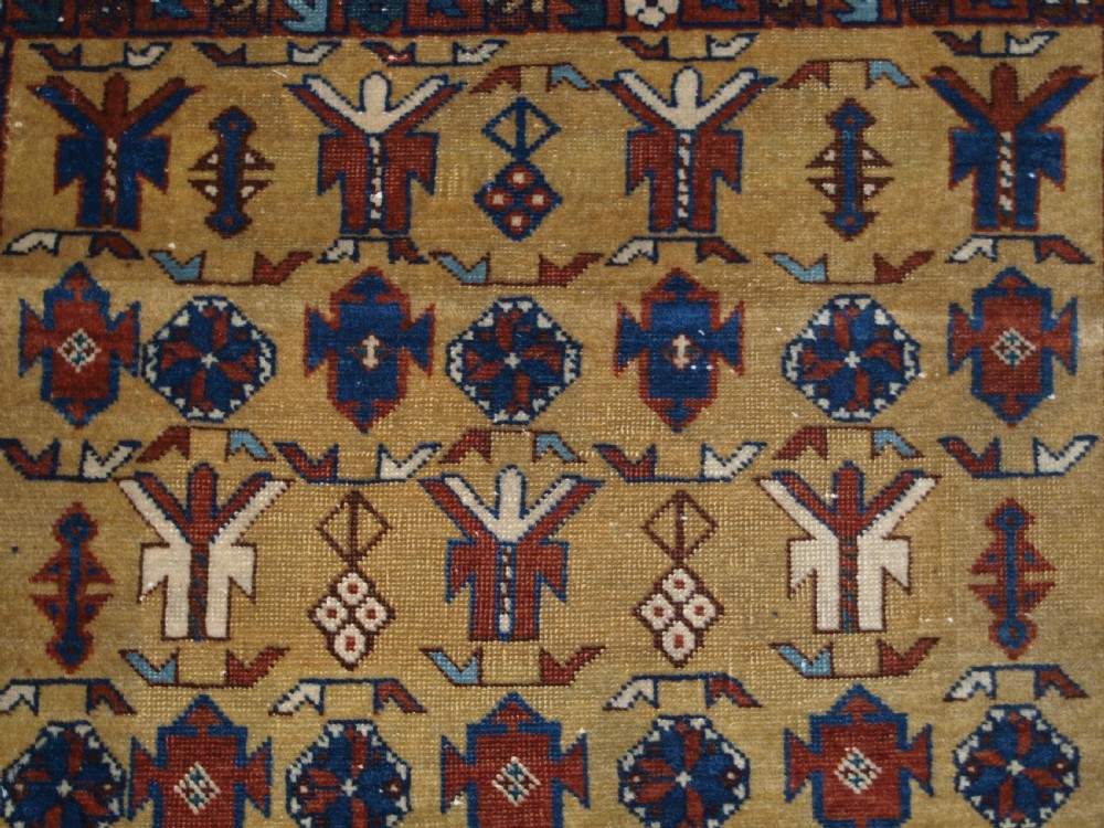 A hand-knotted wool rug featuring a central yellow field decorated with geometric motifs, enclosed by multi-tiered navy blue and terracotta patterned borders. View VII