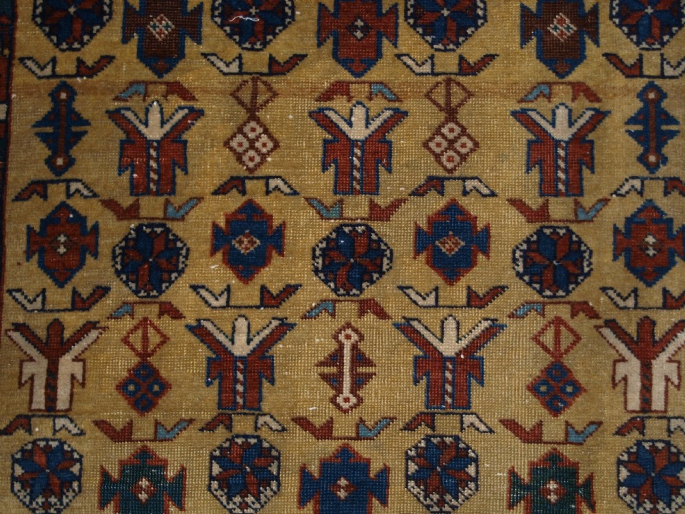 A hand-knotted wool rug featuring a central yellow field decorated with geometric motifs, enclosed by multi-tiered navy blue and terracotta patterned borders. View VIII