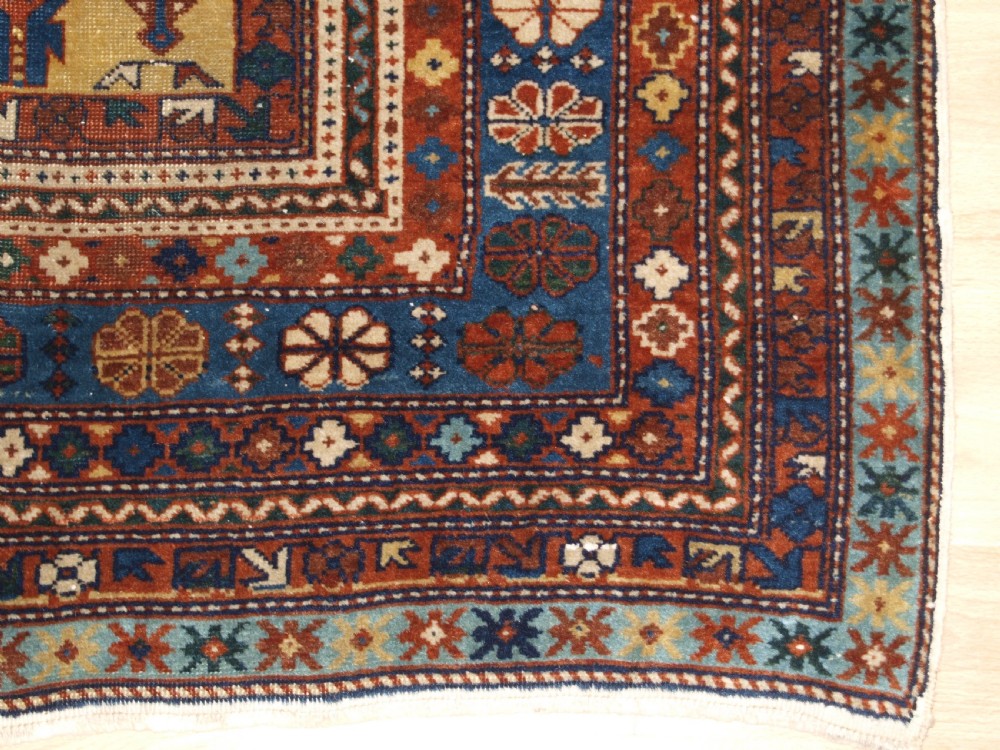 A hand-knotted wool rug featuring a central yellow field decorated with geometric motifs, enclosed by multi-tiered navy blue and terracotta patterned borders. View IX