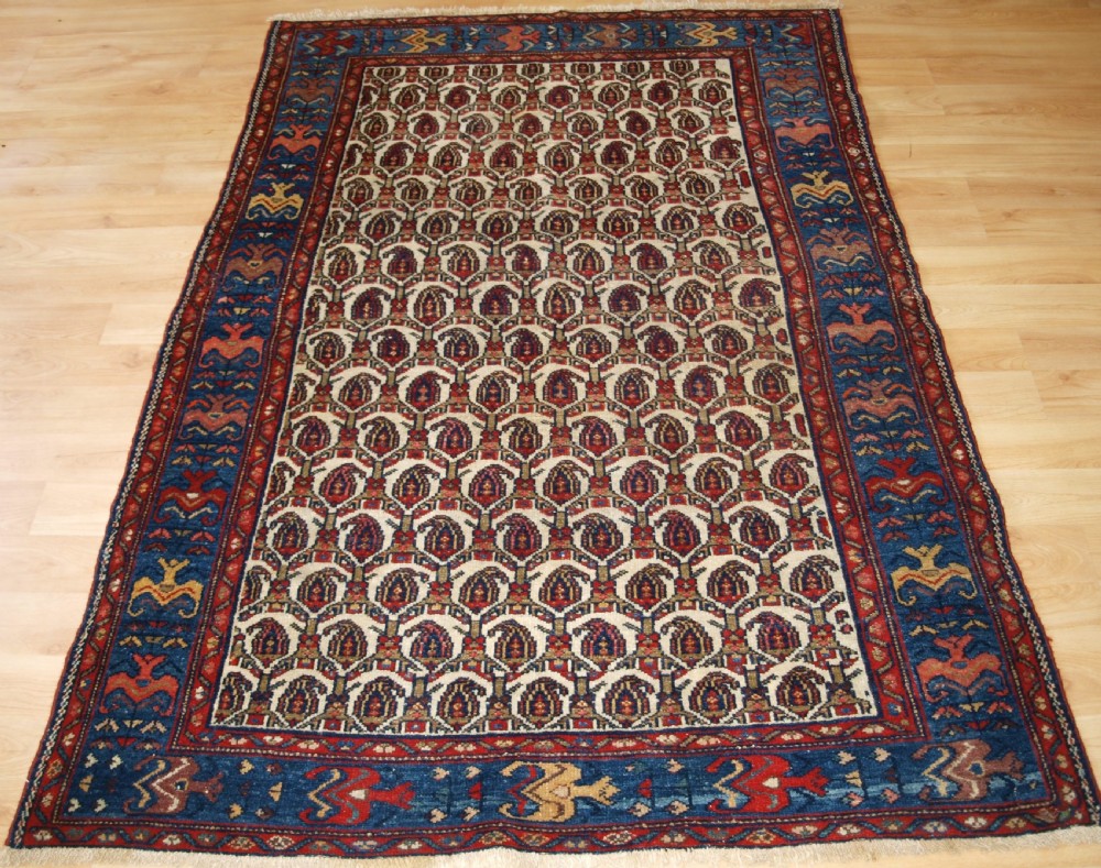 An antique Hamadan hand-knotted wool rug featuring a repeating boteh pattern on an ivory field surrounded by a deep blue border with stylized motifs.