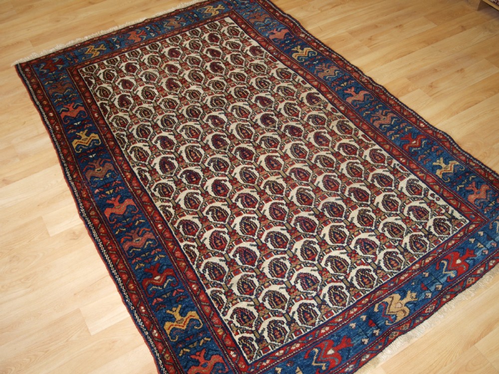 An antique Hamadan hand-knotted wool rug featuring a repeating boteh pattern on an ivory field surrounded by a deep blue border with stylized motifs. View II