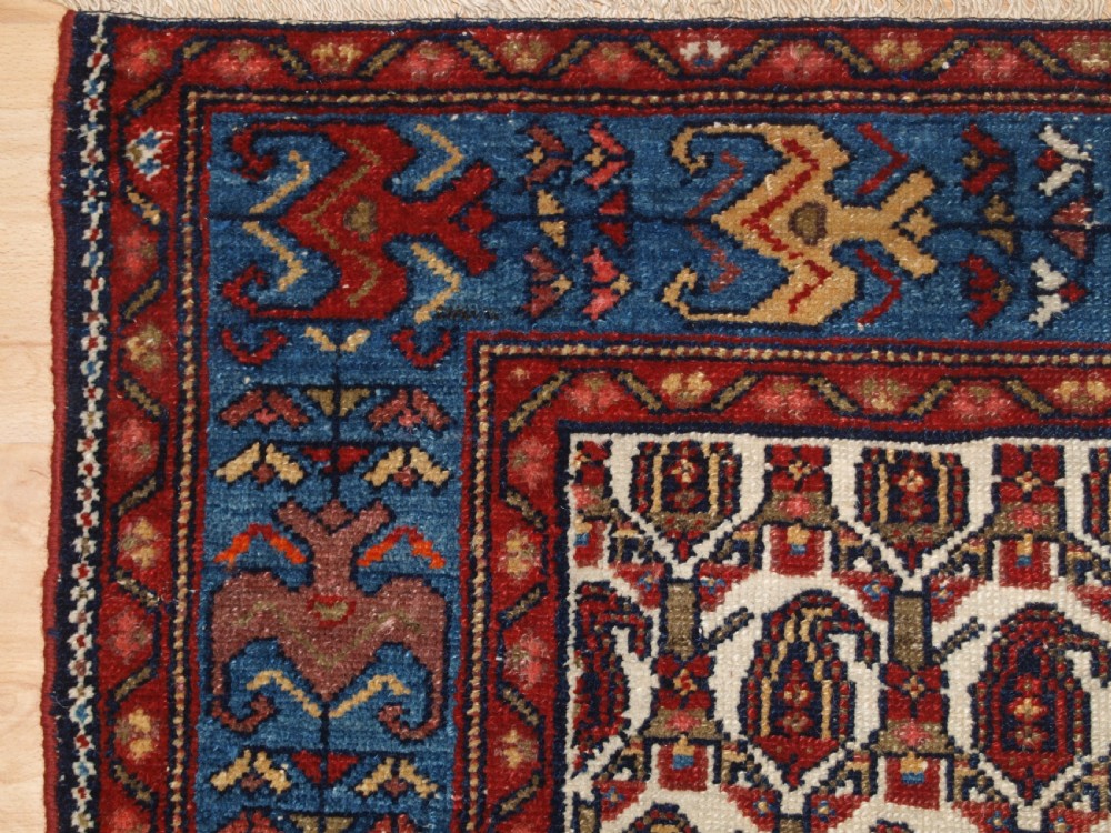 An antique Hamadan hand-knotted wool rug featuring a repeating boteh pattern on an ivory field surrounded by a deep blue border with stylized motifs. View III