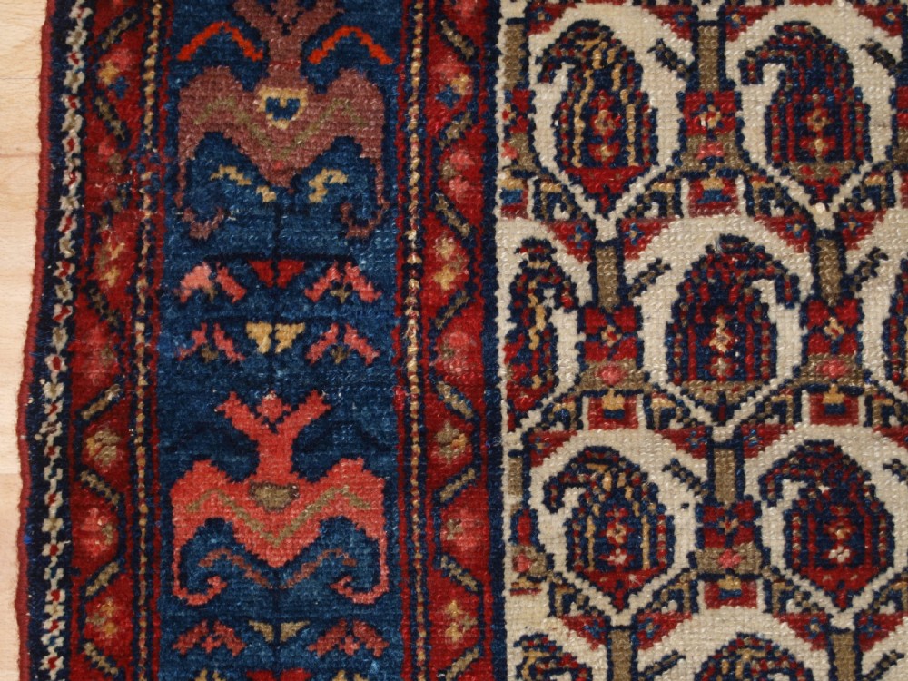 An antique Hamadan hand-knotted wool rug featuring a repeating boteh pattern on an ivory field surrounded by a deep blue border with stylized motifs. View IV