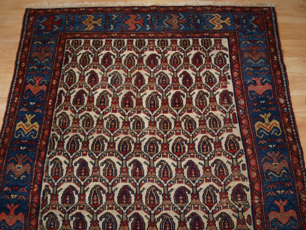 An antique Hamadan hand-knotted wool rug featuring a repeating boteh pattern on an ivory field surrounded by a deep blue border with stylized motifs. View V