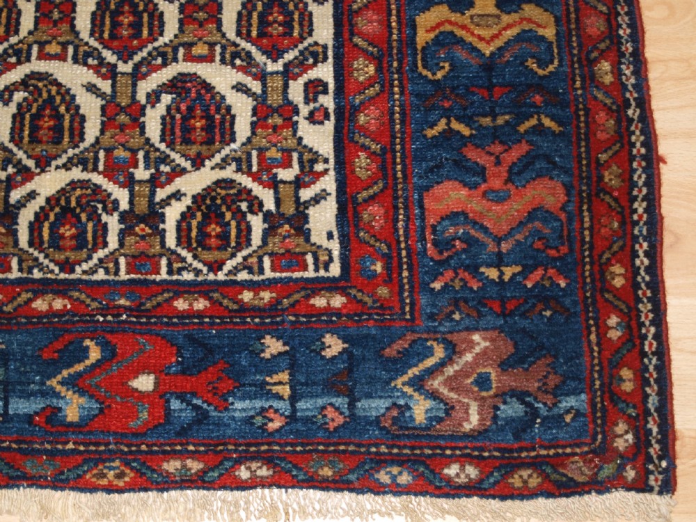 An antique Hamadan hand-knotted wool rug featuring a repeating boteh pattern on an ivory field surrounded by a deep blue border with stylized motifs. View X