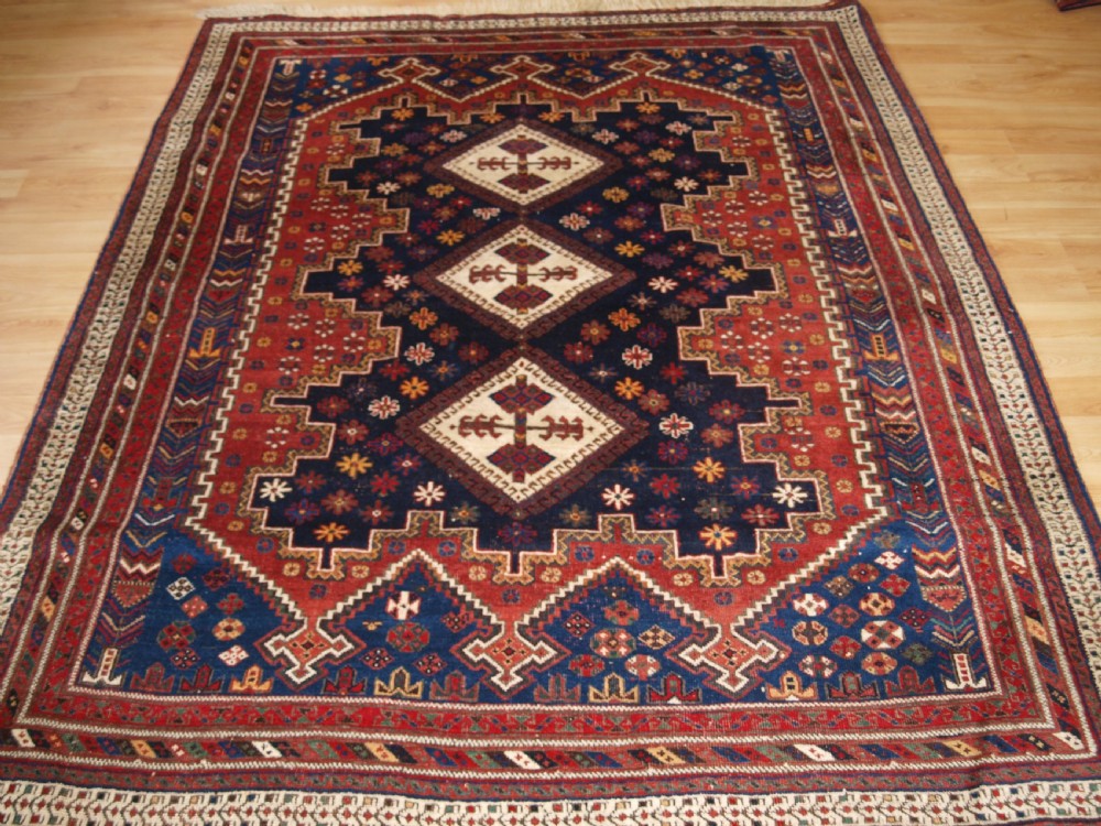 A hand-knotted antique Persian Afshar rug featuring three stacked diamond medallions surrounded by geometric floral motifs in navy blue, terracotta red, and ivory tones.